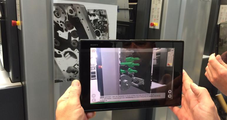 HÃ¤nde halten Tablet vor Druckmaschine, um mit Hilfe von Augmented Reality einen Blick ins Innere der Maschine zu erlangen